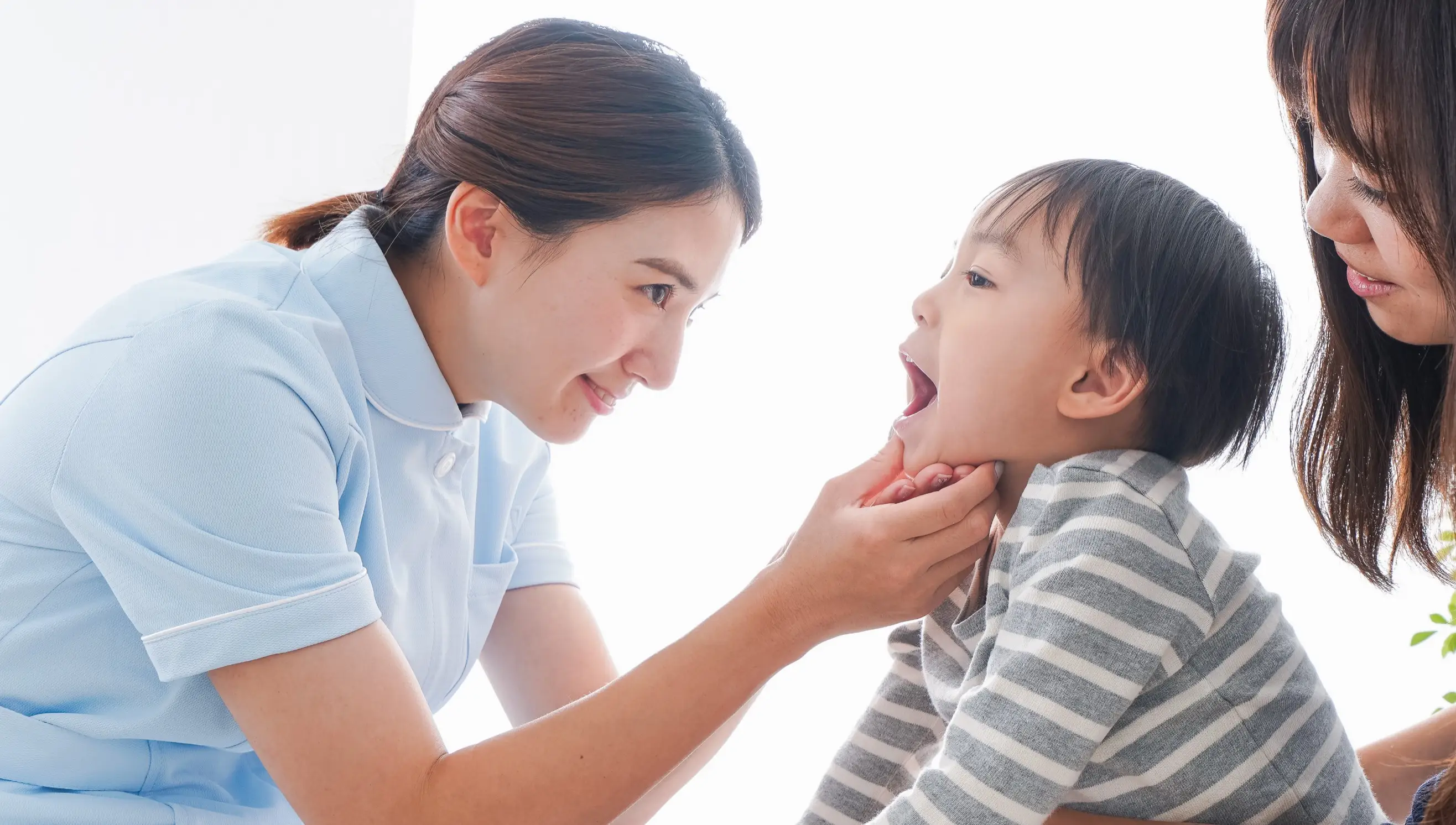 歯科衛生士が母親に付き添われた子どもの口元を優しく診ている様子
