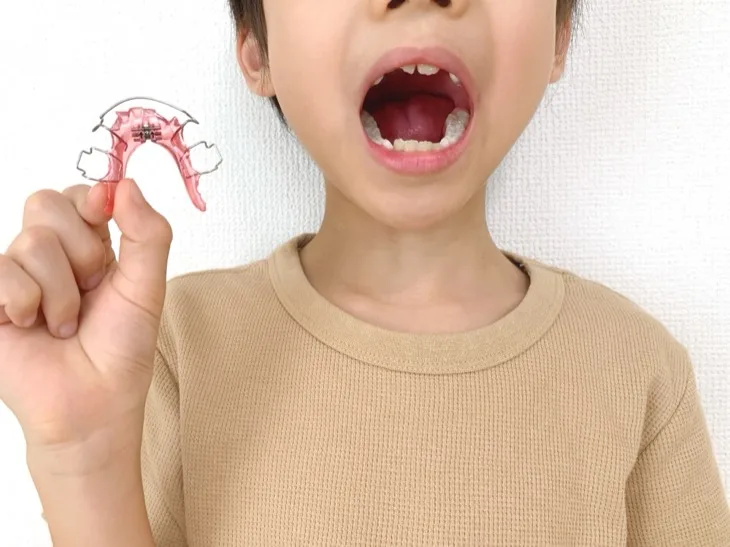 子どもが小児矯正の装置を手に持って口を開けている様子