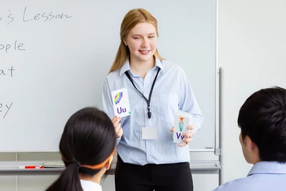 女性講師がアルファベットのカードを持って生徒に話しかけている写真