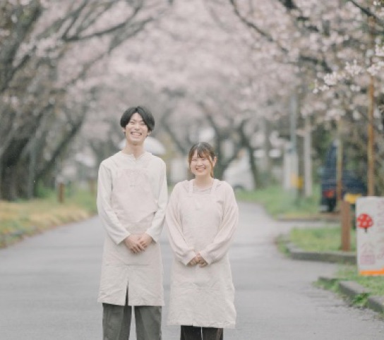 加工前。雨で色がくすんだ桜並木に並んで立つ2人の写真