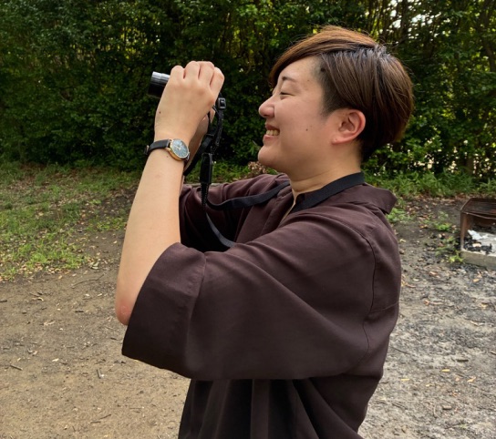 加工前。木の多い公園でカメラを構えている女性の写真