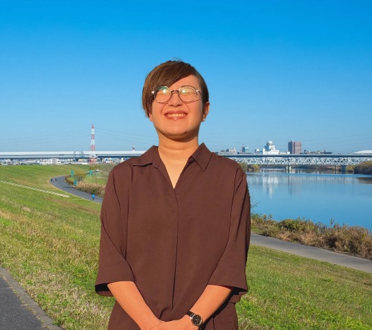 加工後。同じ人物を切り抜き、青空の河川敷と街並みの背景に合成した写真