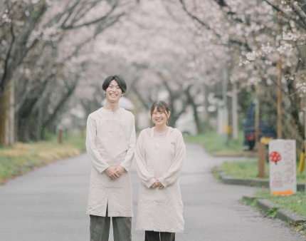 桜並木の下に立つ店主夫婦の写真（加工前）