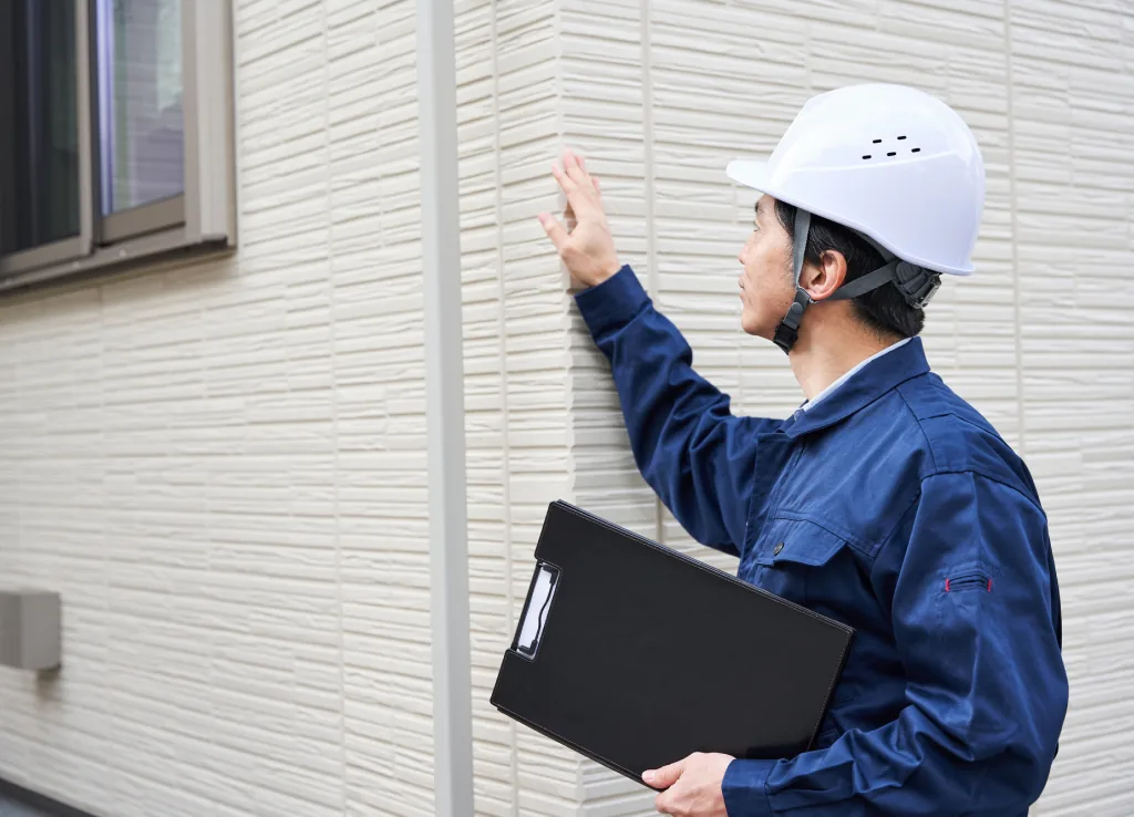 白いヘルメットをかぶり外壁の状態を確かめる現場監督